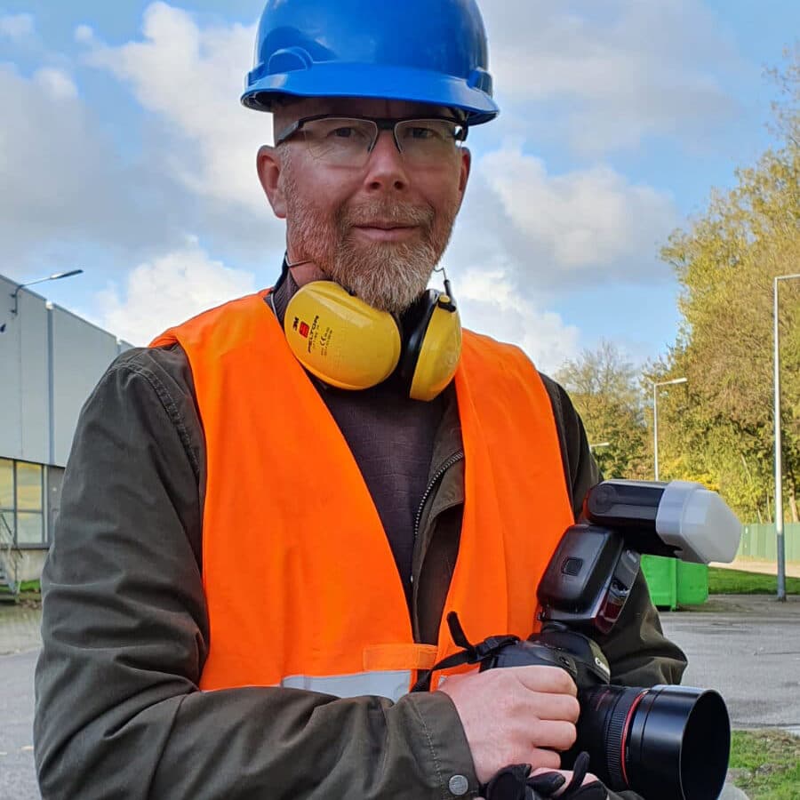 Ted Walker met camera, blauwe helm en veiligheidshesje tijdens een bedrijfsreportage