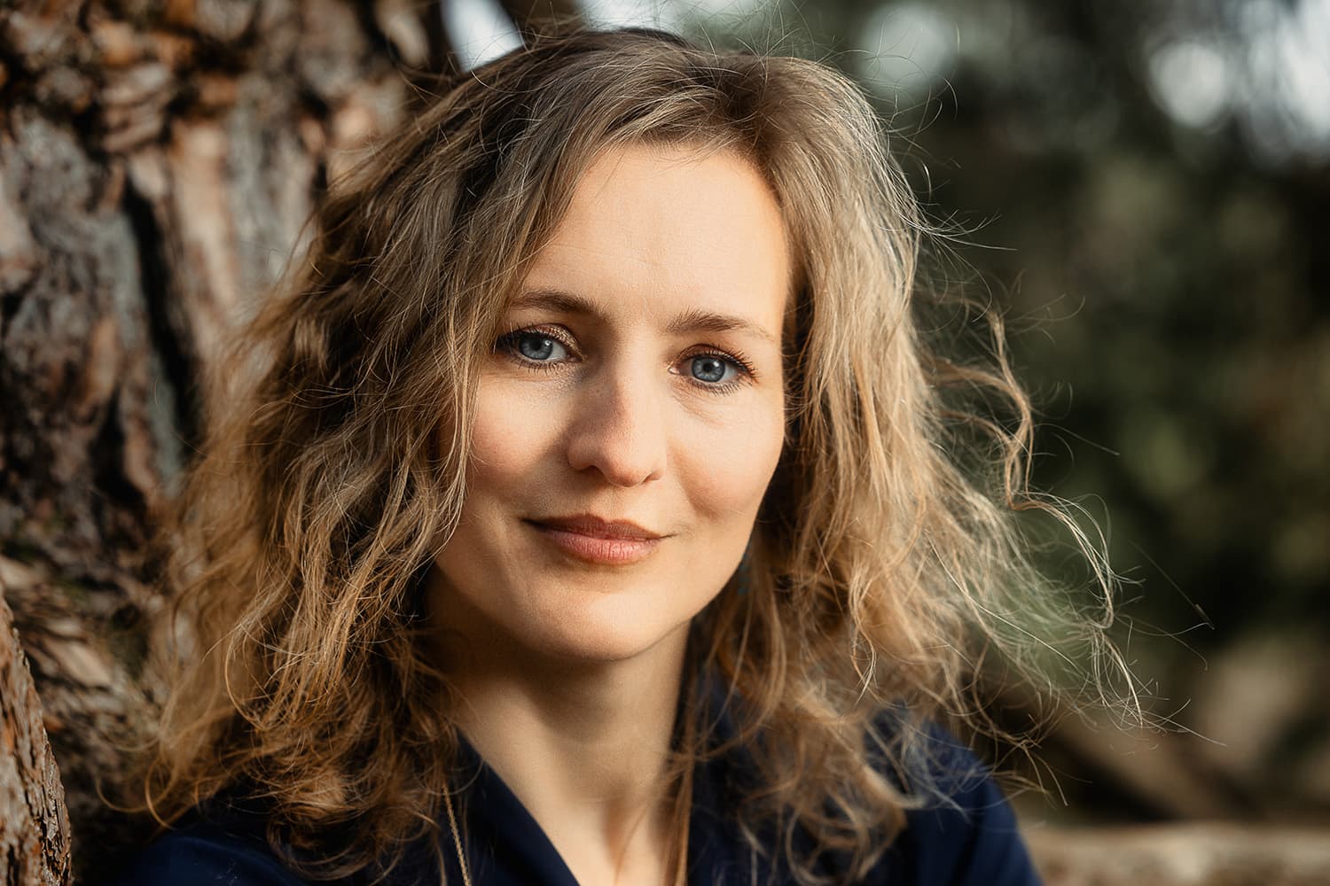 Portret van een vrouw met blond krullend haar bij een boom tijdens een vriendinnenfotoshoot