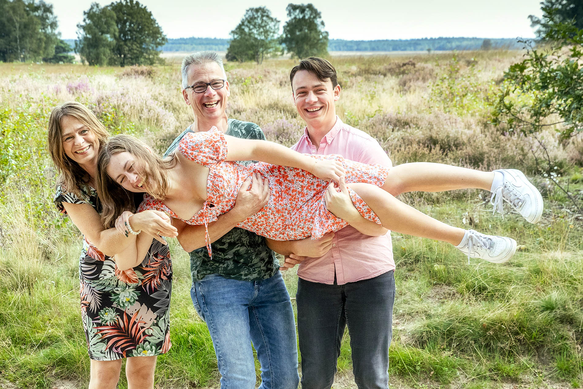 Lachende familie tilt hun dochter op tijdens een fotoshoot op de heide